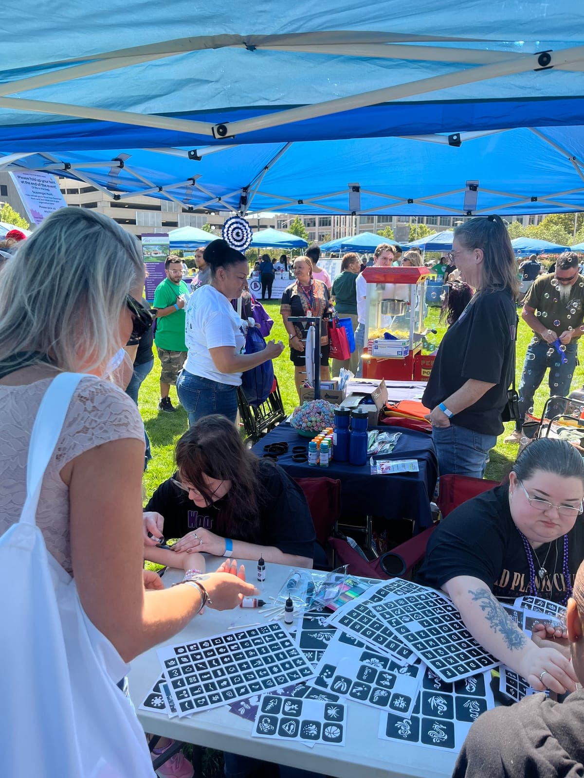 Visitors at an activity table under a blue tent at an outdoor event.