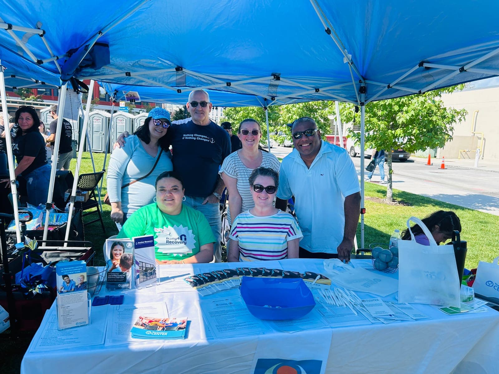 A group of people at an outreach table under a tent at an outdoor event.