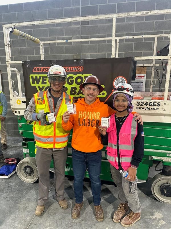 Three construction workers holding up small kit boxes in front of a We've Got Your Back banner